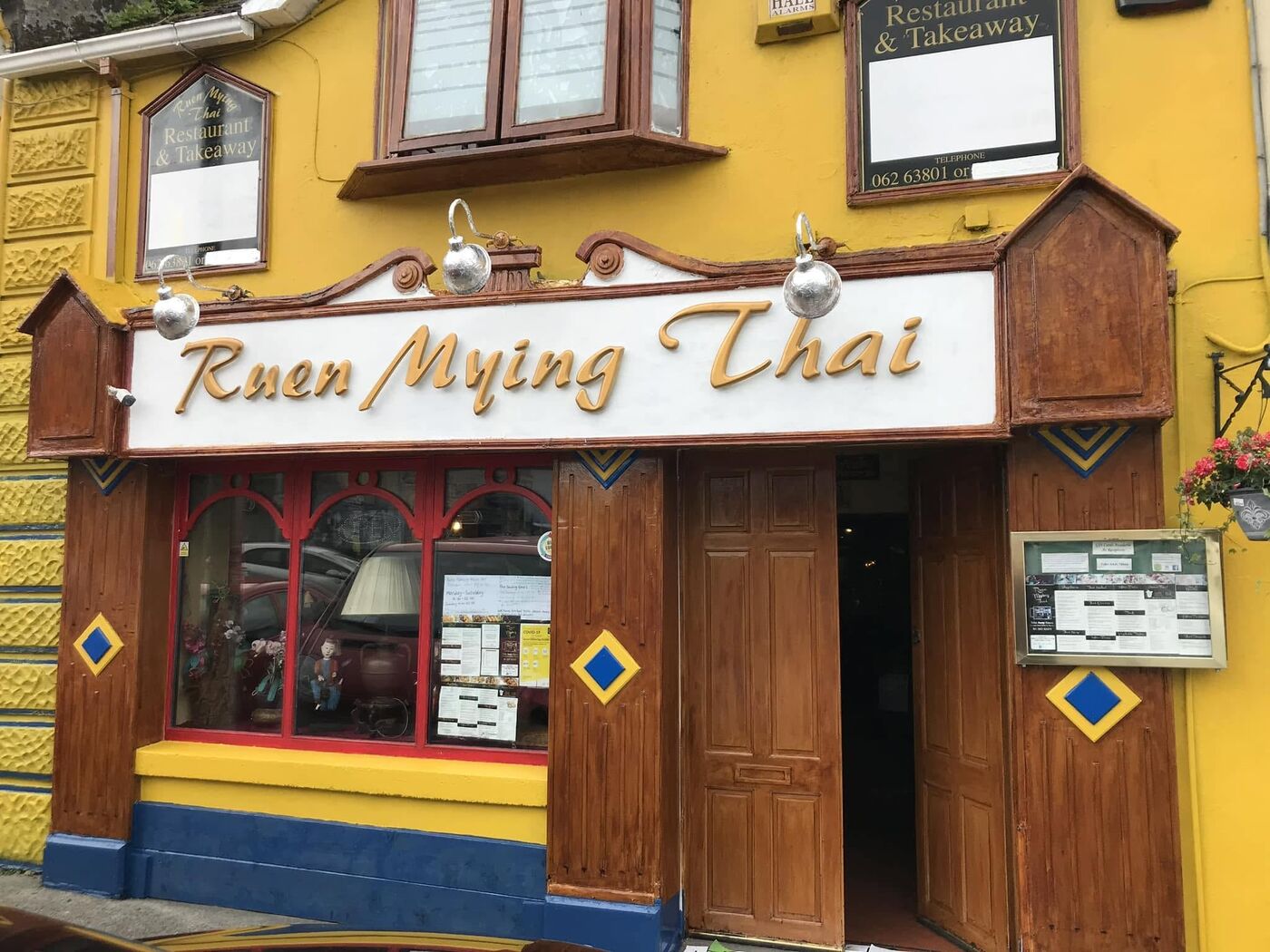 The Ruen Mying Thai shopfront: a yellow wall, wooden doors, blue diamond tiles and a white sign with gold letters
